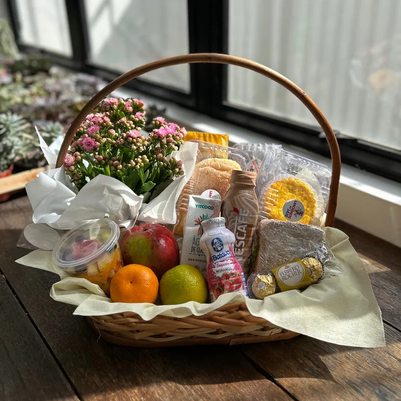 Cesta de café da manhã em vime com flor, frutas e itens de padaria da JC Flores